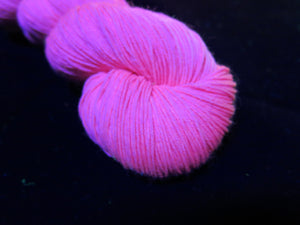 hand dyed solid bubblegum pink yarn fluorescing under uv black light