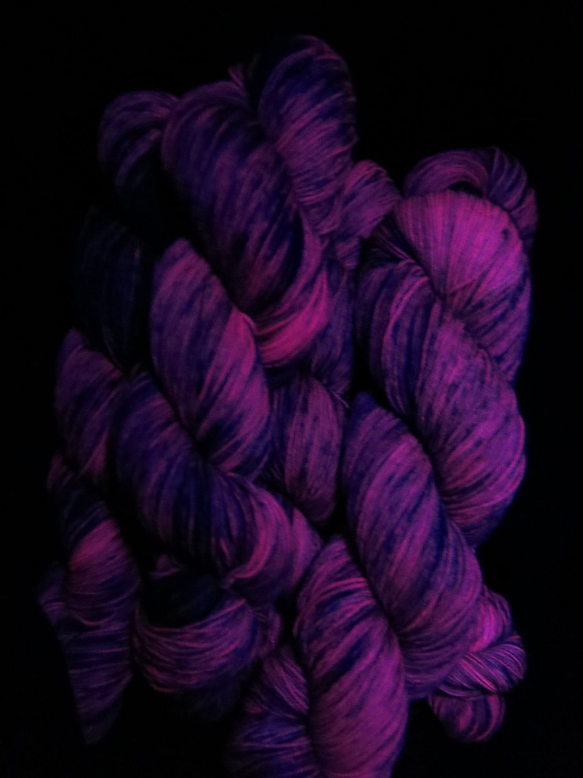 purple speckled sock yarn fluorescing under uv black light