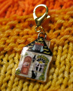 enamel stitich marker on a gold clasp with a cottage door with a black cat on step